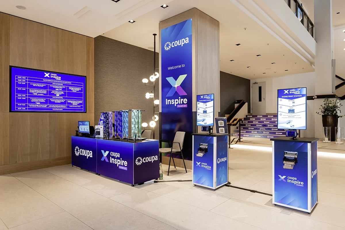 Veranstaltungsbereich mit blauem Coupa Inspire-Branding, Infotafeln, Stehtischen und Treppe mit Markenaufdruck