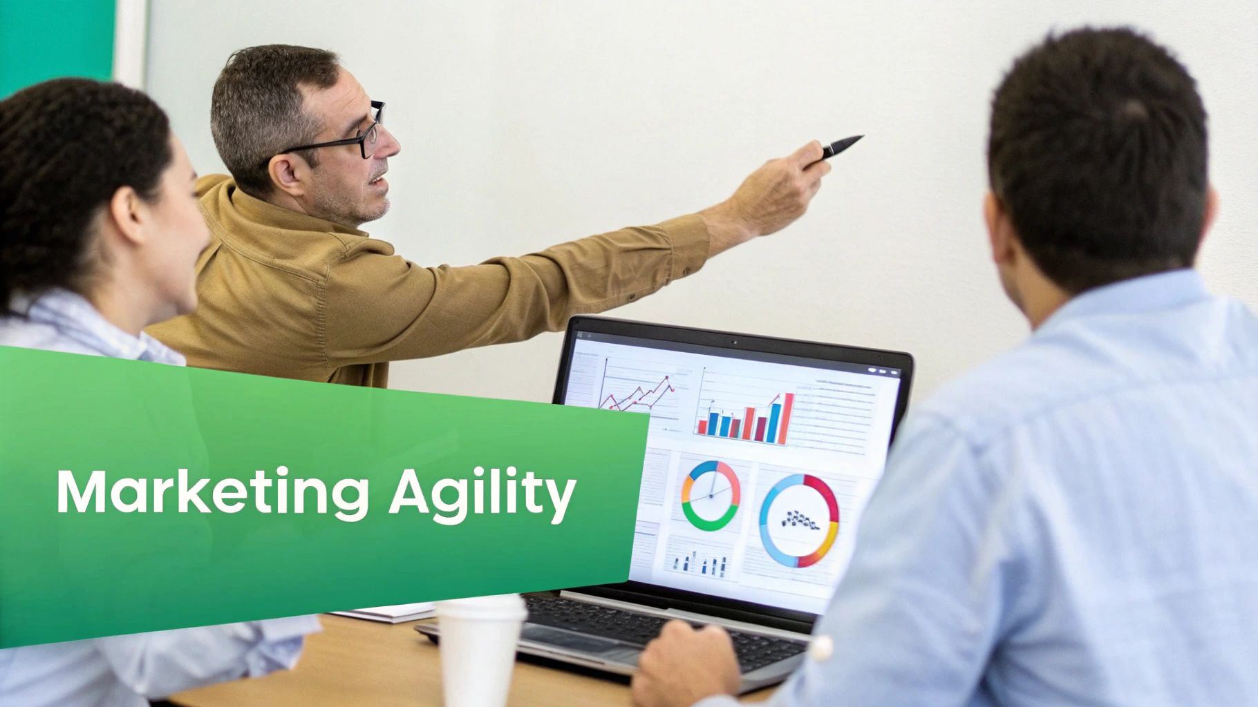 Three professionals discuss marketing agility in an office, with one presenting and another analyzing data on a laptop.