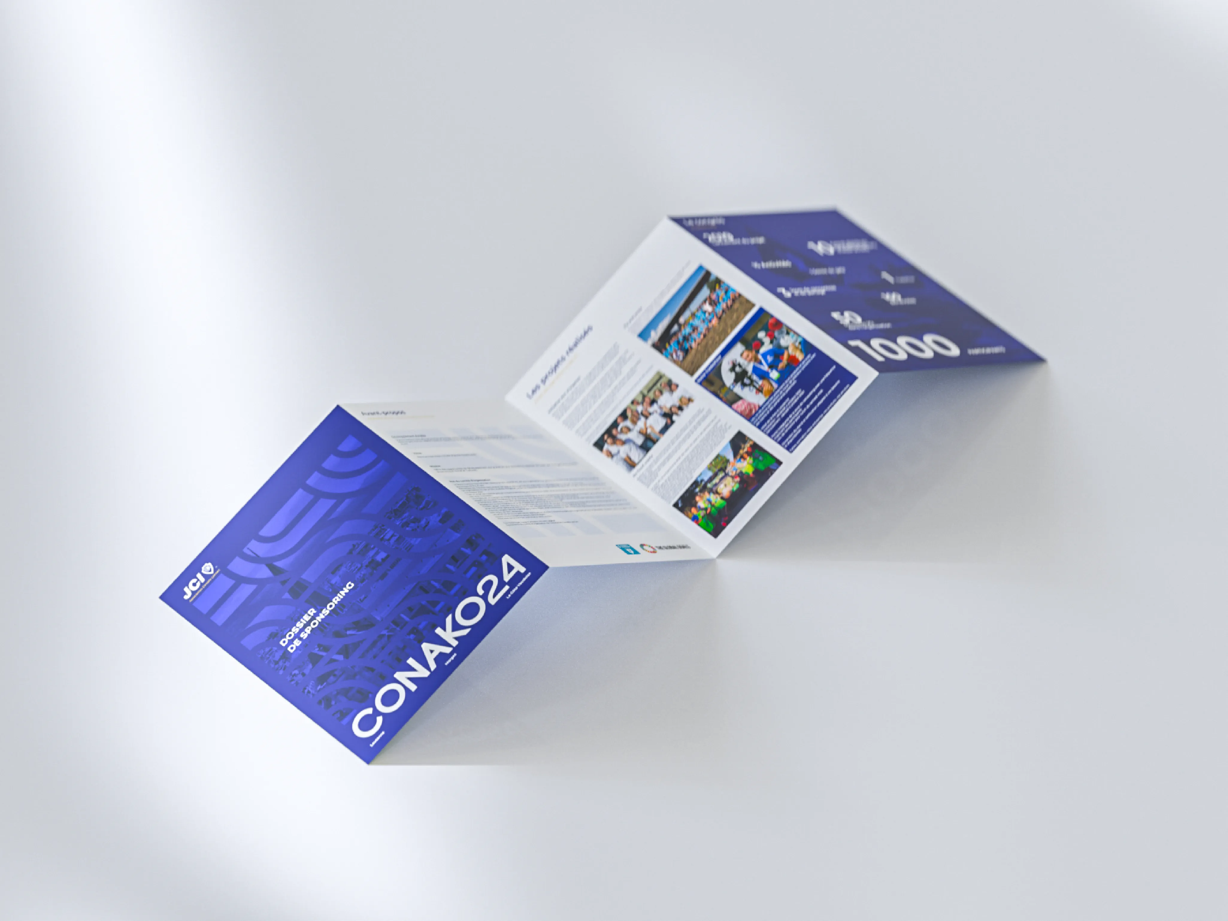 Brochure ouverte à plusieurs volets avec couverture bleue intitulée CONAKO24 et texte en français, posée sur une surface claire.