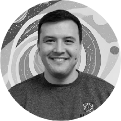 Smiling man with short dark hair wearing a dark crewneck sweater in front of an abstract circular patterned background.