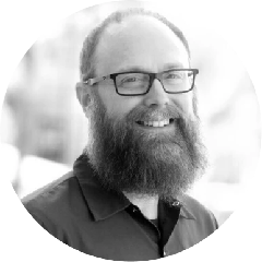 Smiling man with glasses and a full beard wearing a collared shirt.