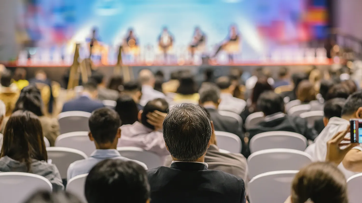 Hybrid event scene showing a busy conference hall with a simultaneous live stream audience on screens and mobile apps