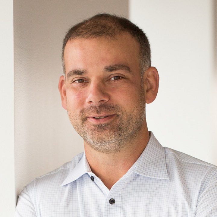 Man with short hair and beard wearing white checkered shirt