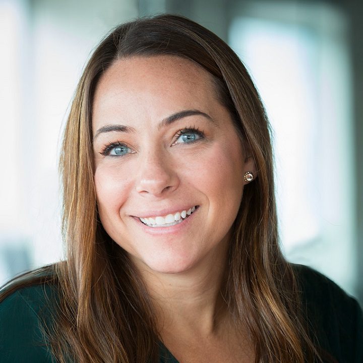 Professional headshot of smiling woman with long brown hair against blurred background