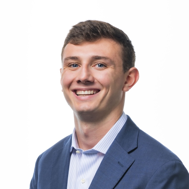 Smiling man in blue blazer and light purple striped shirt, portrait against white background