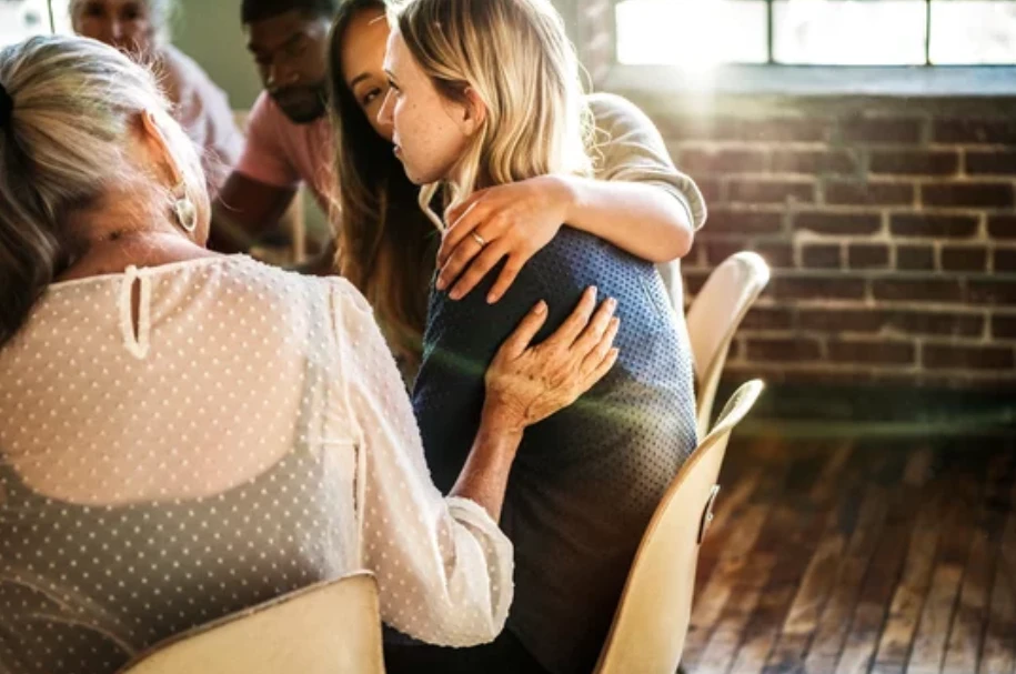 A group seated together, one person embracing another in support