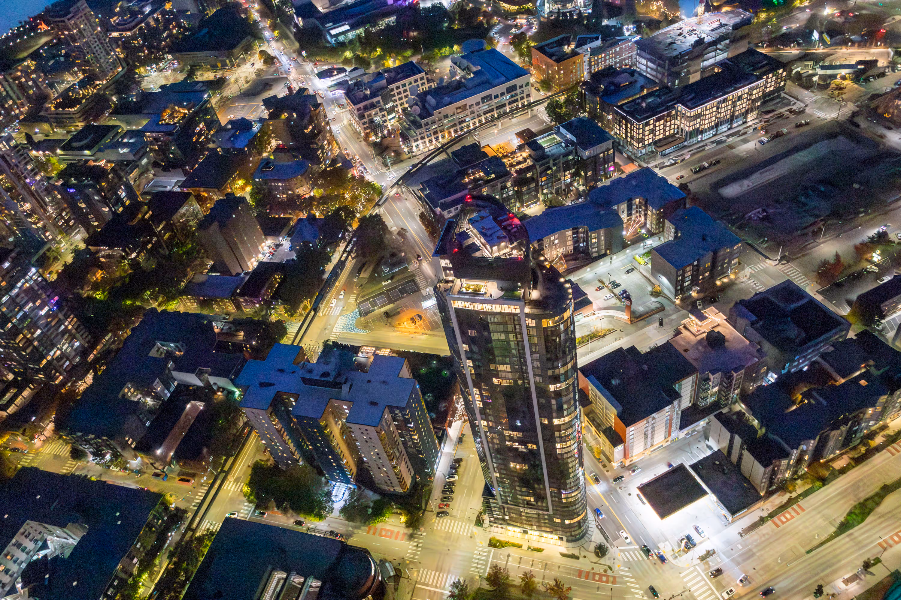 A nighttime aerial photo of a well-lit city street and skyscraper