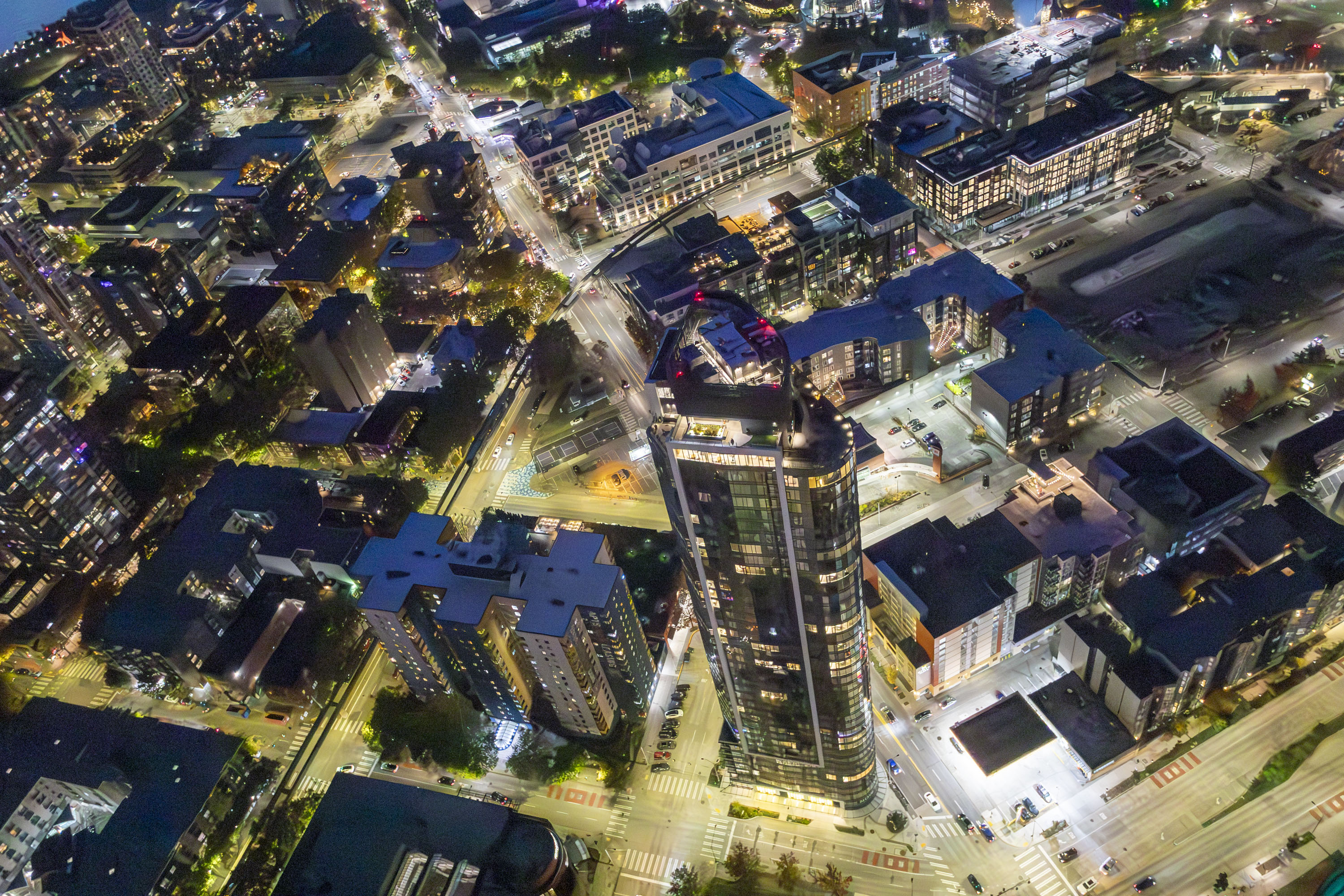 A nighttime aerial photo of a well-lit city street and skyscraper