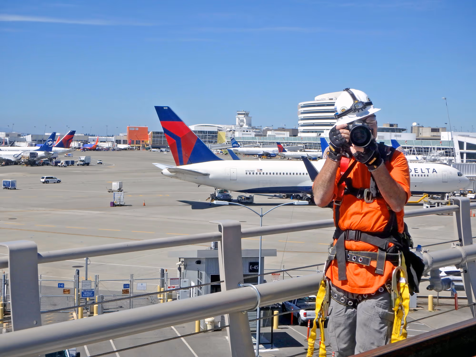 A photographer wearing construction safety equipment taking photos of an airport construction project