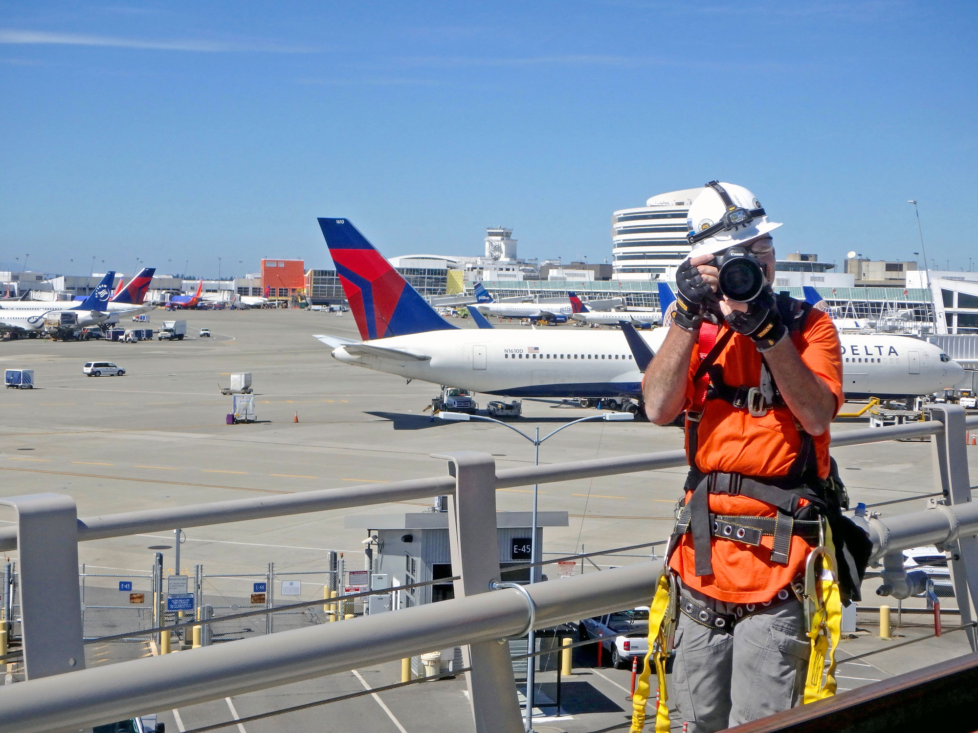 A photographer wearing construction safety equipment taking photos of an airport construction project