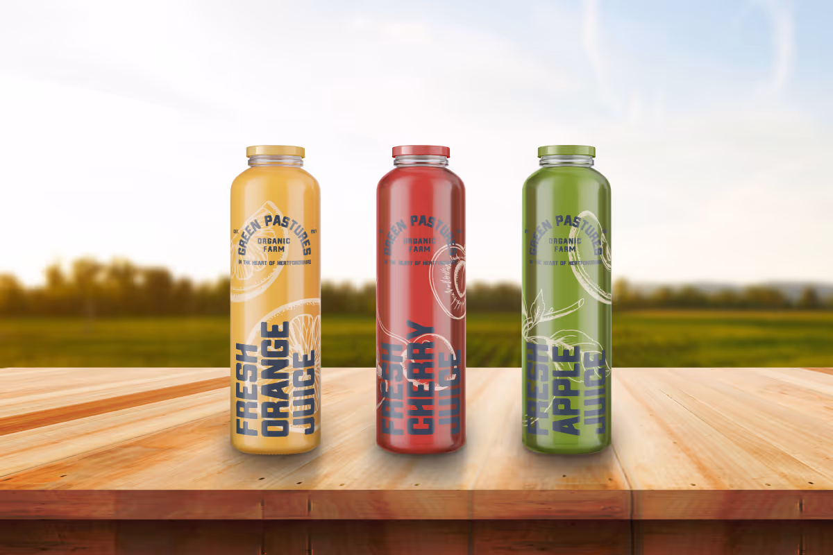 juice design for pure delights. 3 bottles of different flavour juices sat on a table in a field
