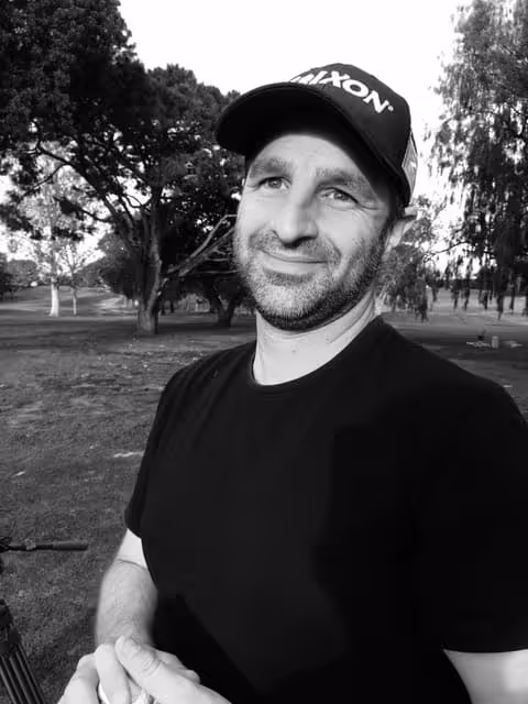 Smiling man in black cap and shirt sitting in park with trees