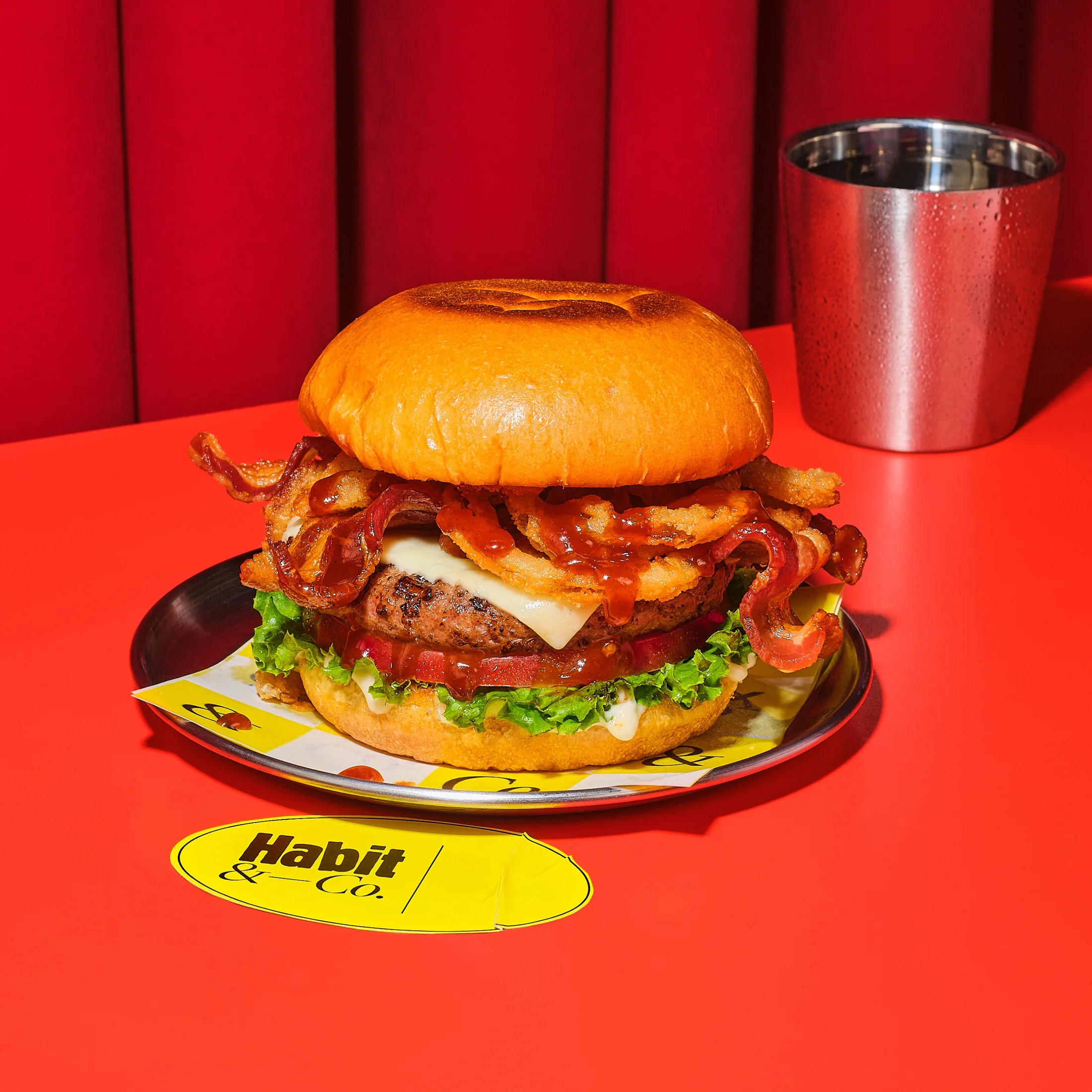 Bacon cheeseburger on a metal plate against a red backdrop