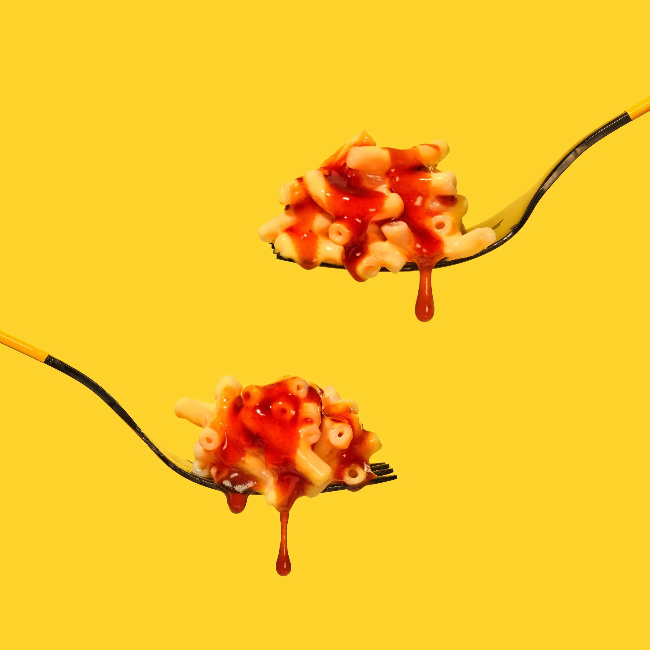 Two forks lifting sweet corn pasta with chilli sauce against a yellow backdrop