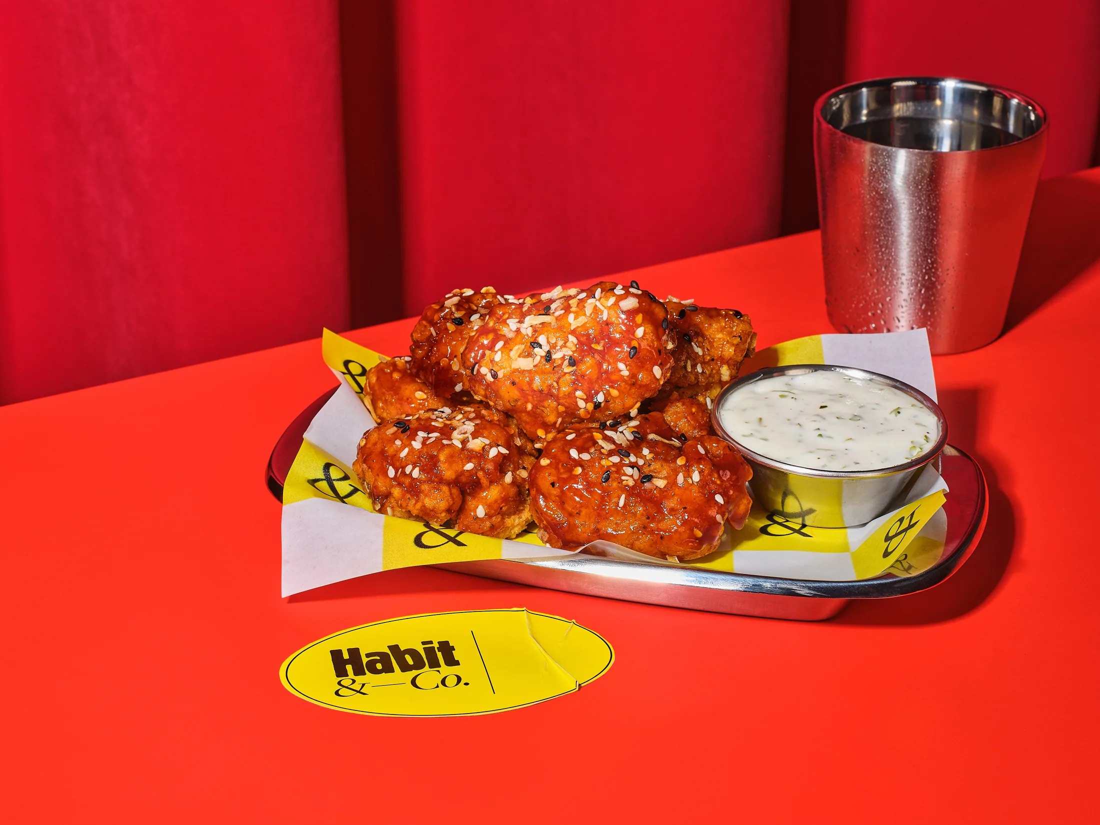 Sesame glazed crispy chicken tenders on a tray with dipping sauce