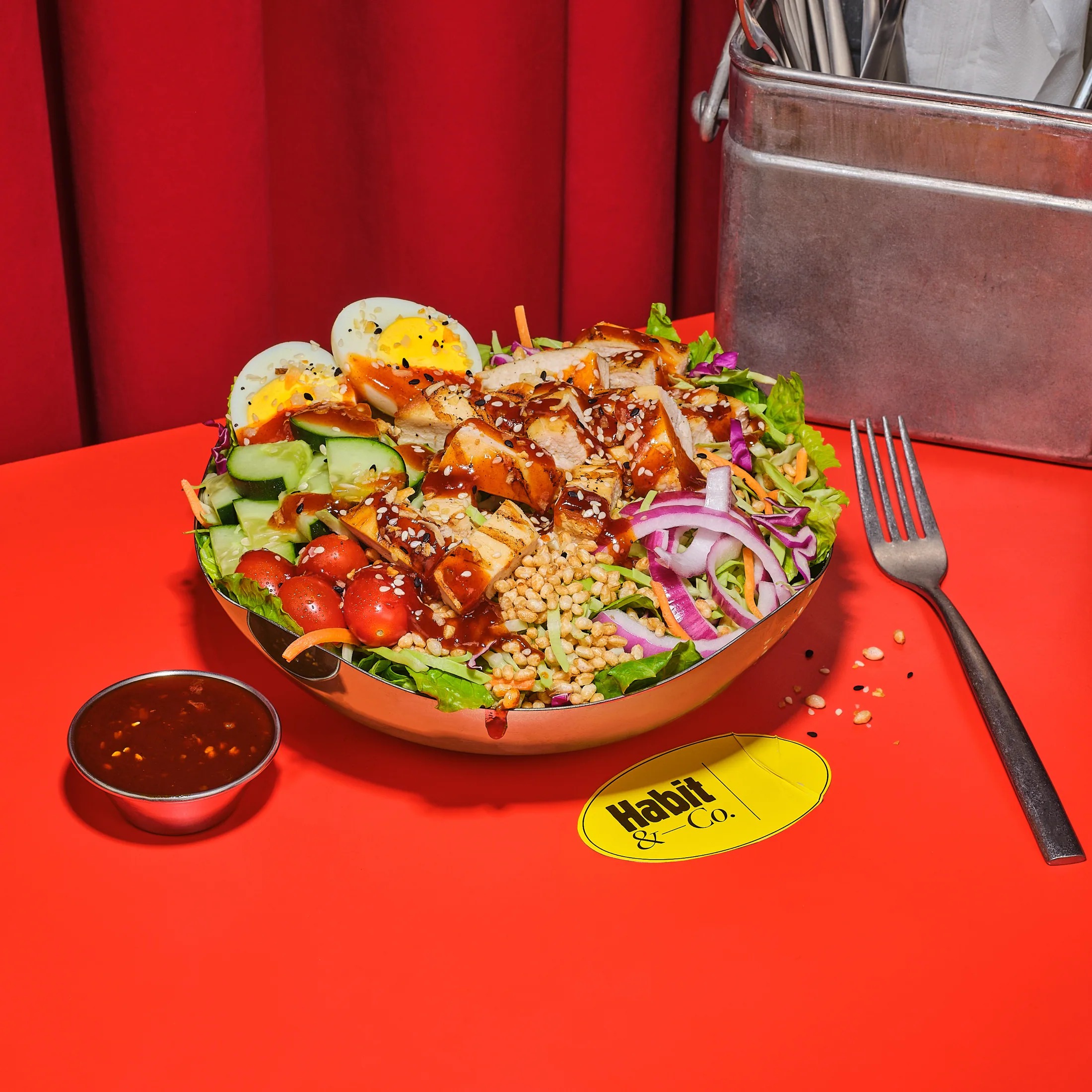 Loaded cobb salad bowl with tomatoes, egg and red onion on a red table