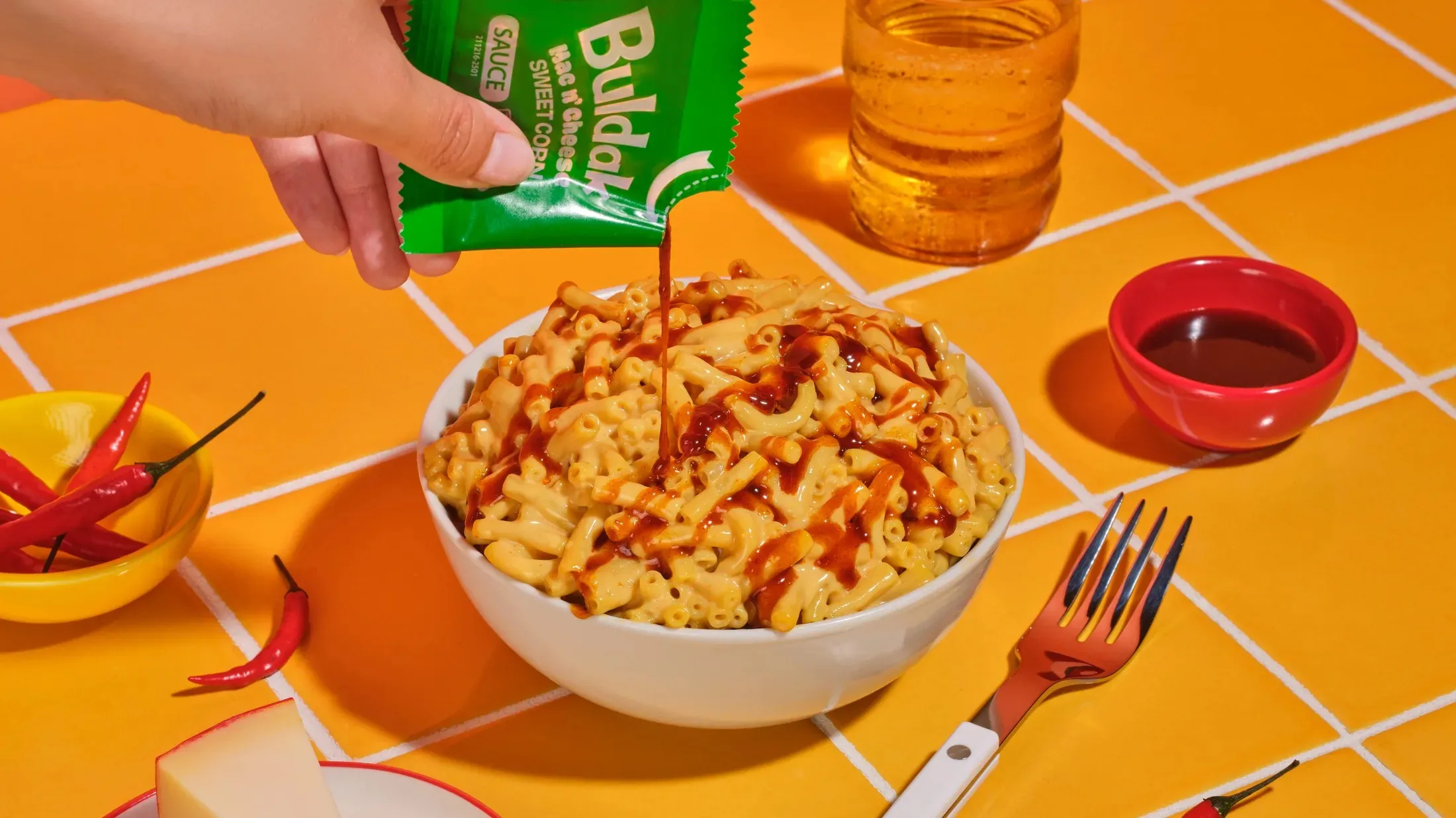 Hand squeezing sauce over a bowl of sweet corn pasta on a yellow tiled table