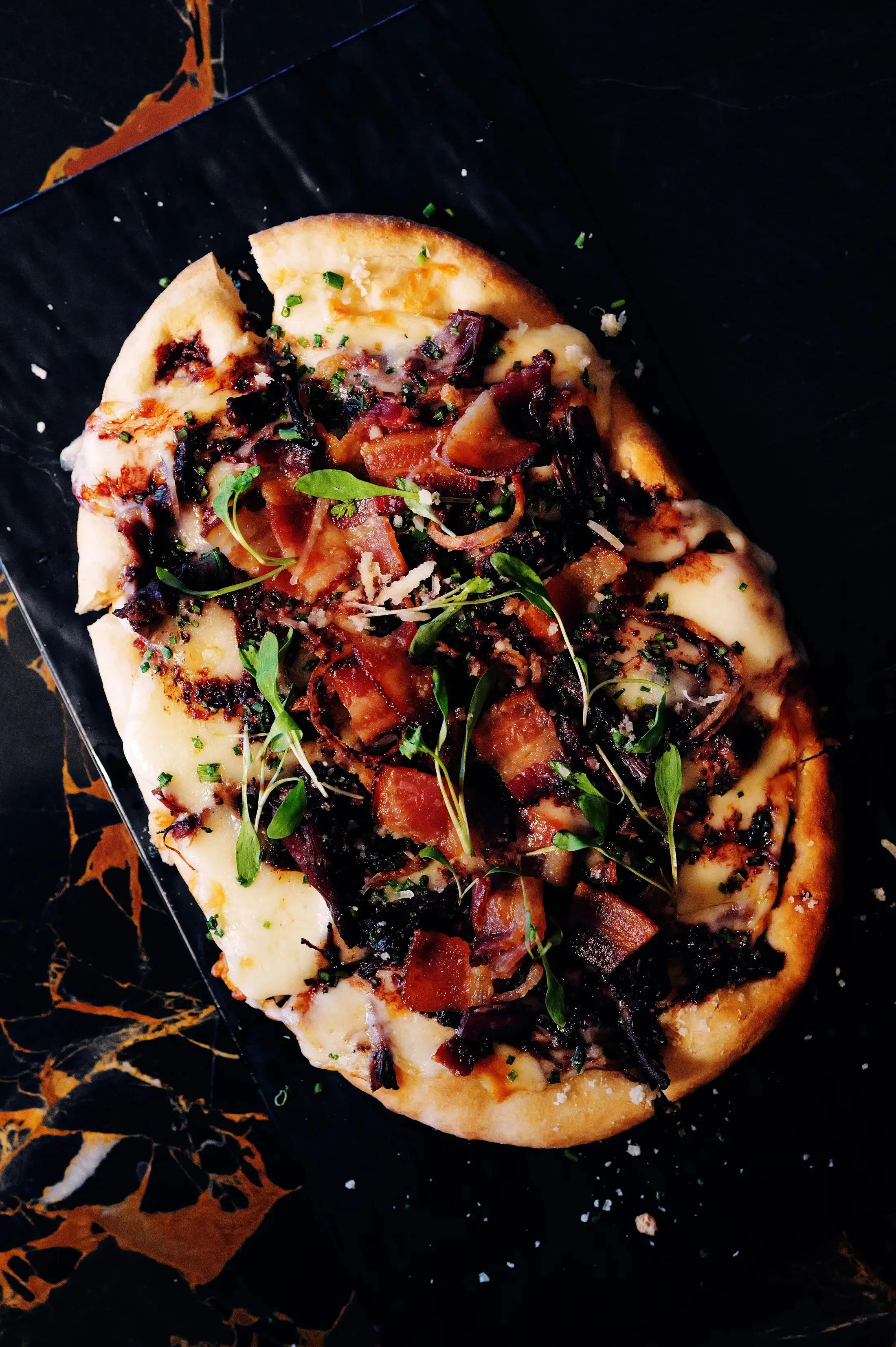 Flatbread with prosciutto and arugula on dark slate