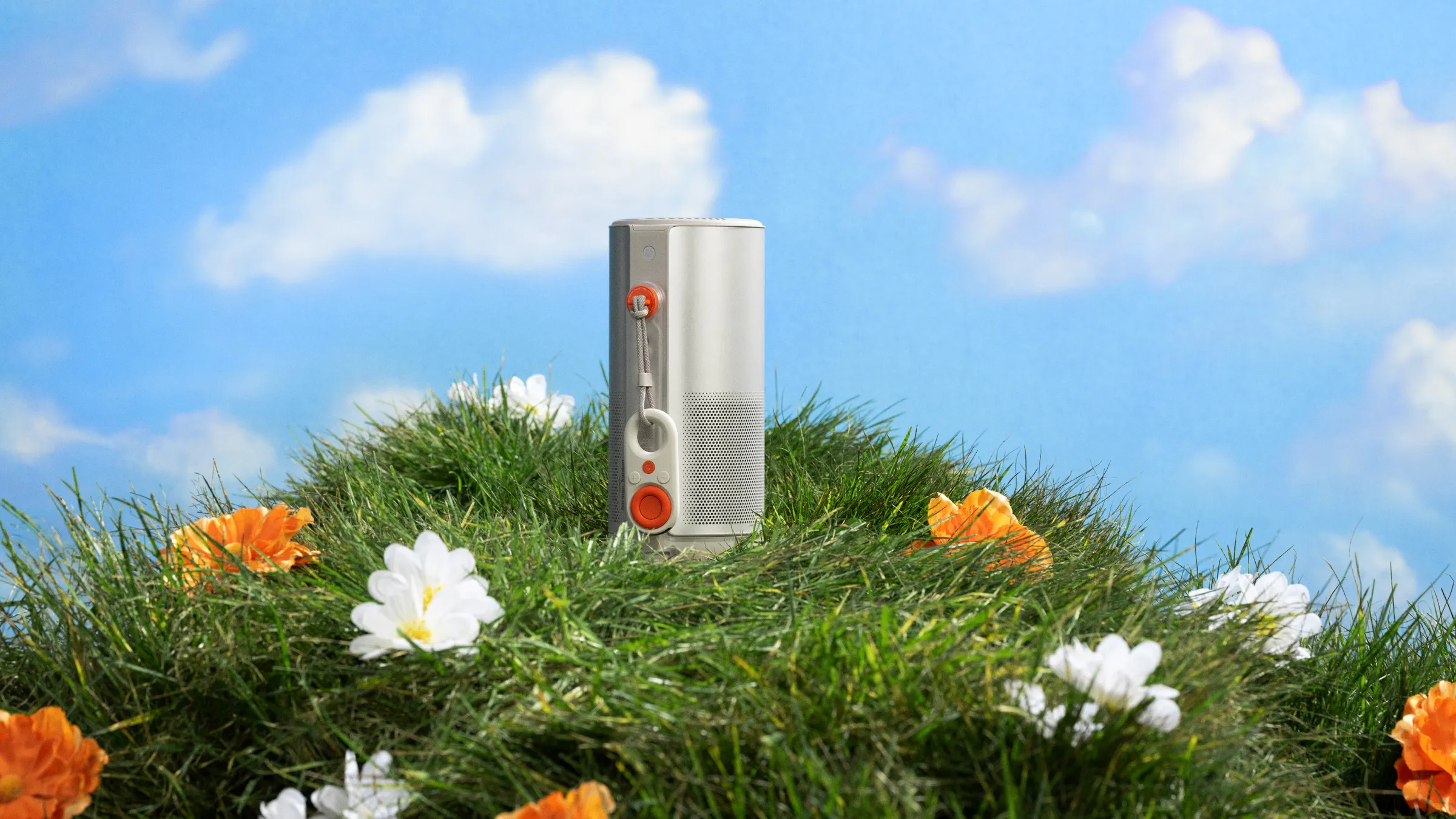 XGIMI MoGo projector standing on a grassy mound scattered with orange and white flowers against a blue sky
