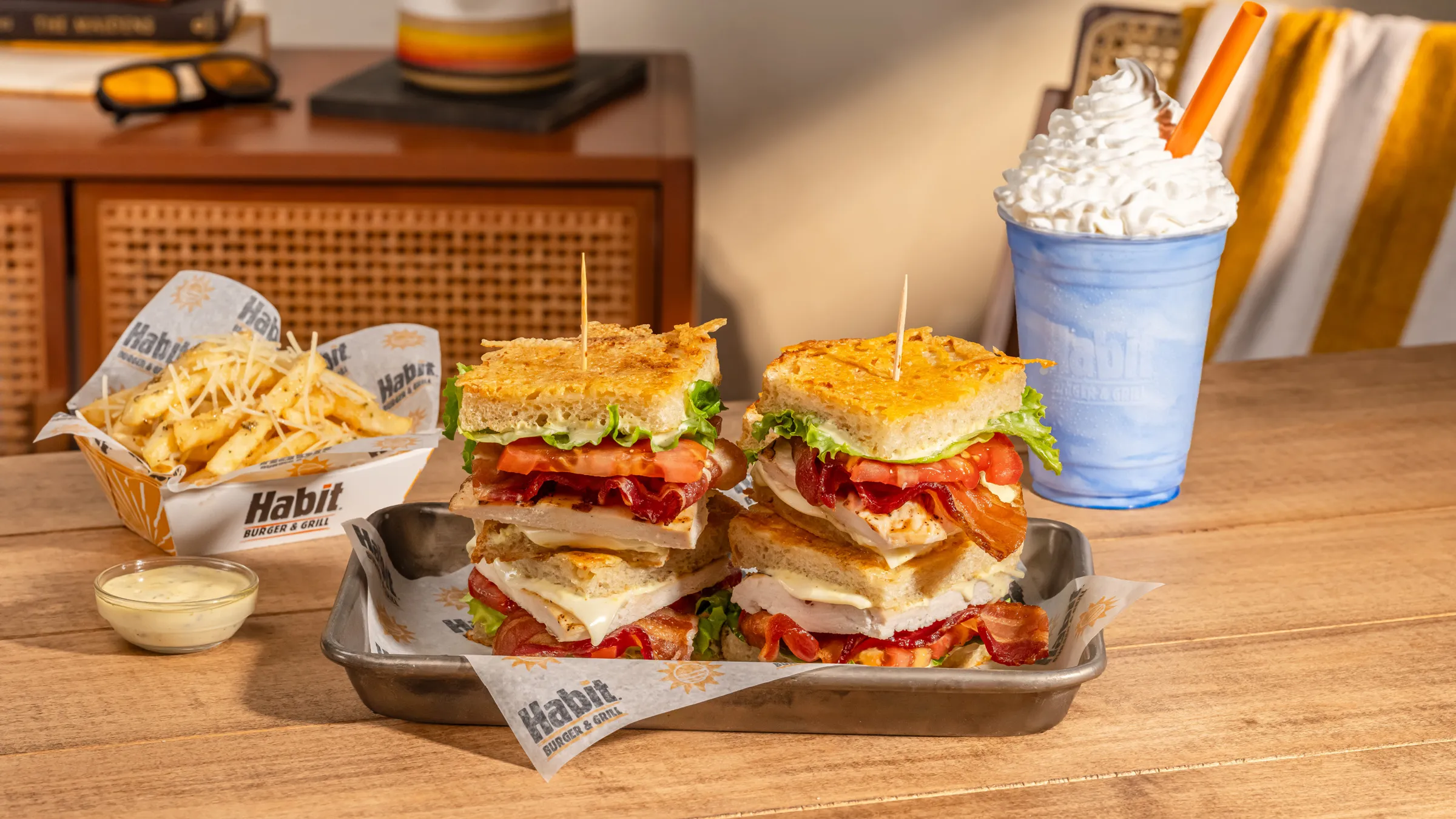 Habit Burger club sandwich halves on a tray with a basket of fries, dipping sauce and a milkshake