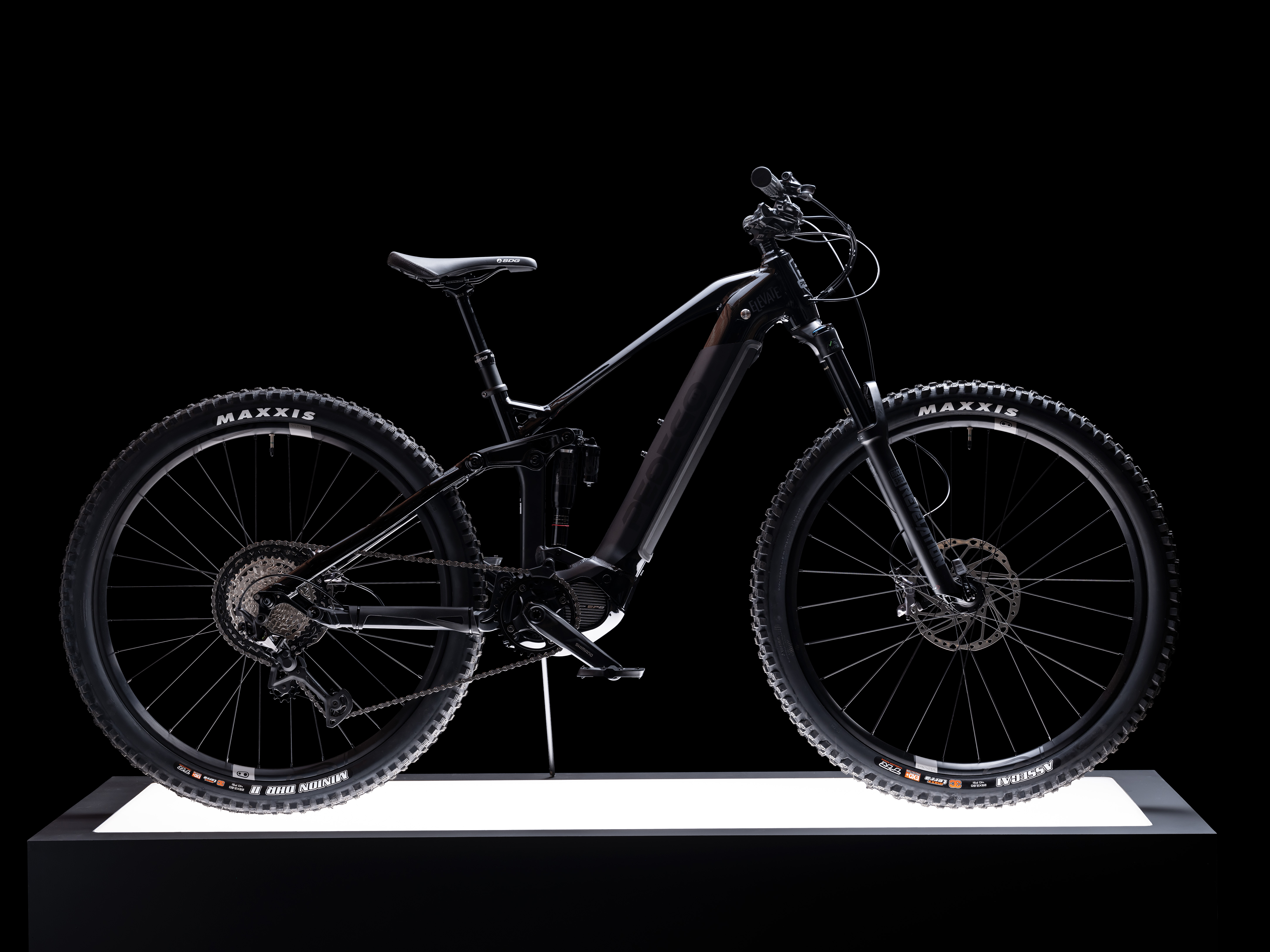 Pedego electric mountain bike displayed side-on atop a lit plinth against a black background