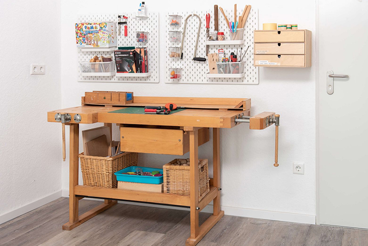 Wooden workbench with tools and supplies organized on pegboards and baskets in a clean workshop room.
