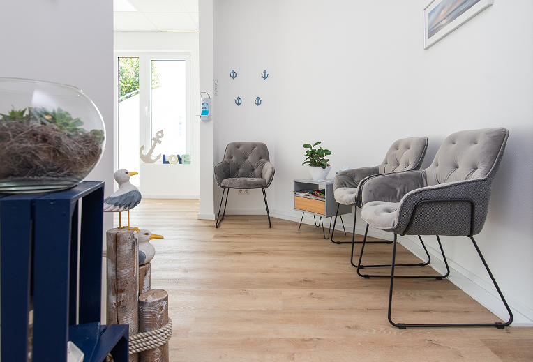 Modern waiting area with three gray cushioned chairs, a small table with a plant, and nautical-themed decorative items on the wall and floor.