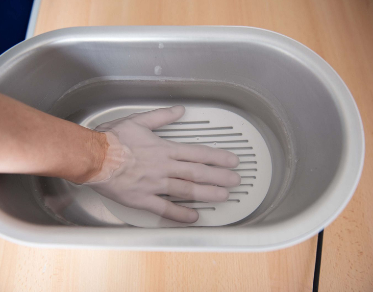 Hand submerged in water inside a gray plastic container on a wooden surface.