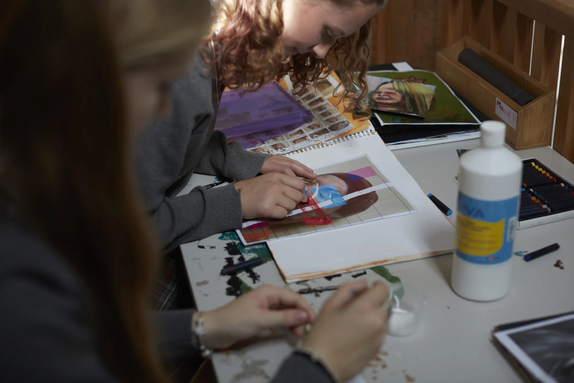 Two people working on an art project with coloured pencils, a ruler, and a sketchbook featuring a face drawing.