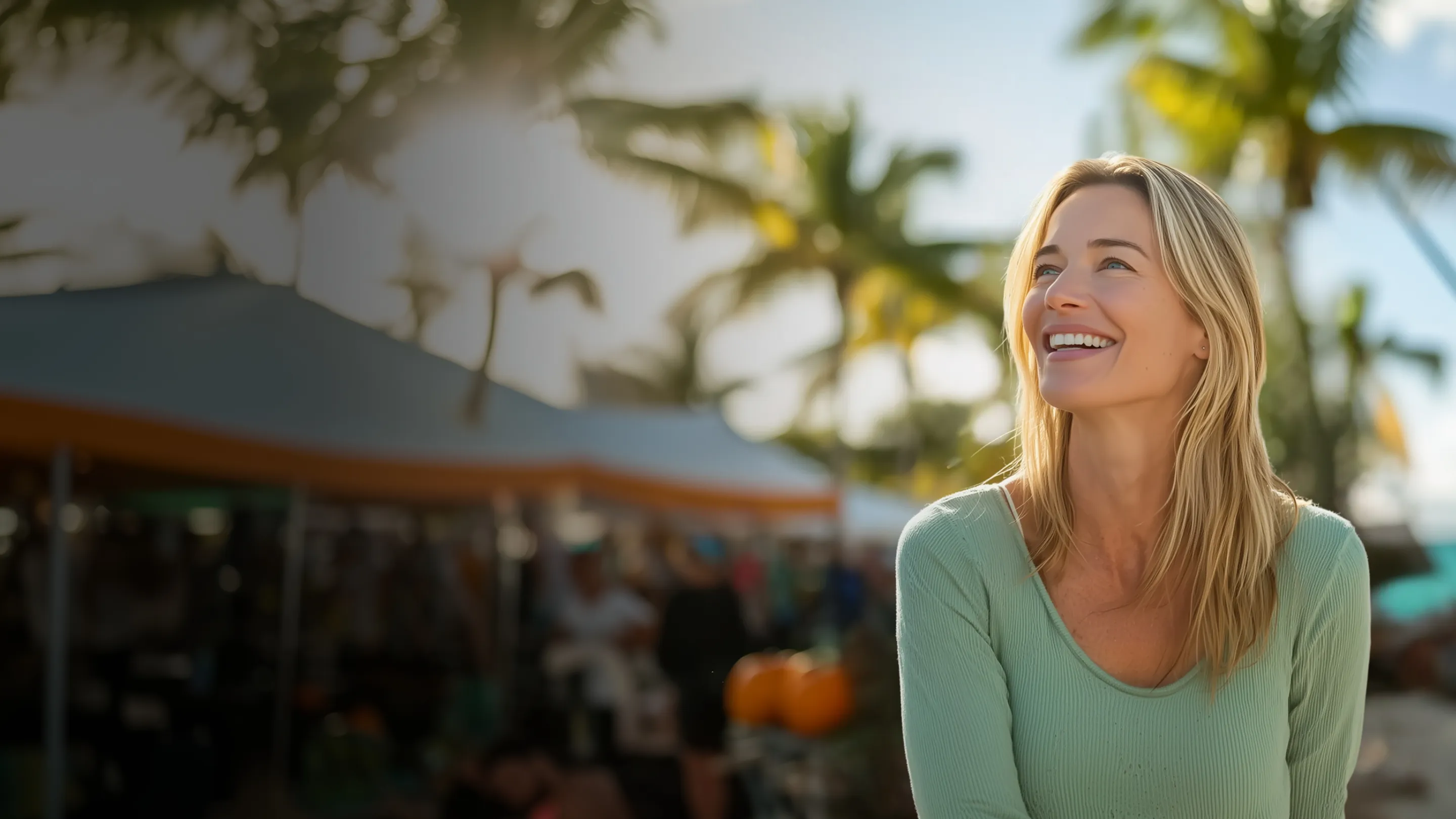 A smiling woman stands in front of lush palm trees, radiating joy in a tropical setting.