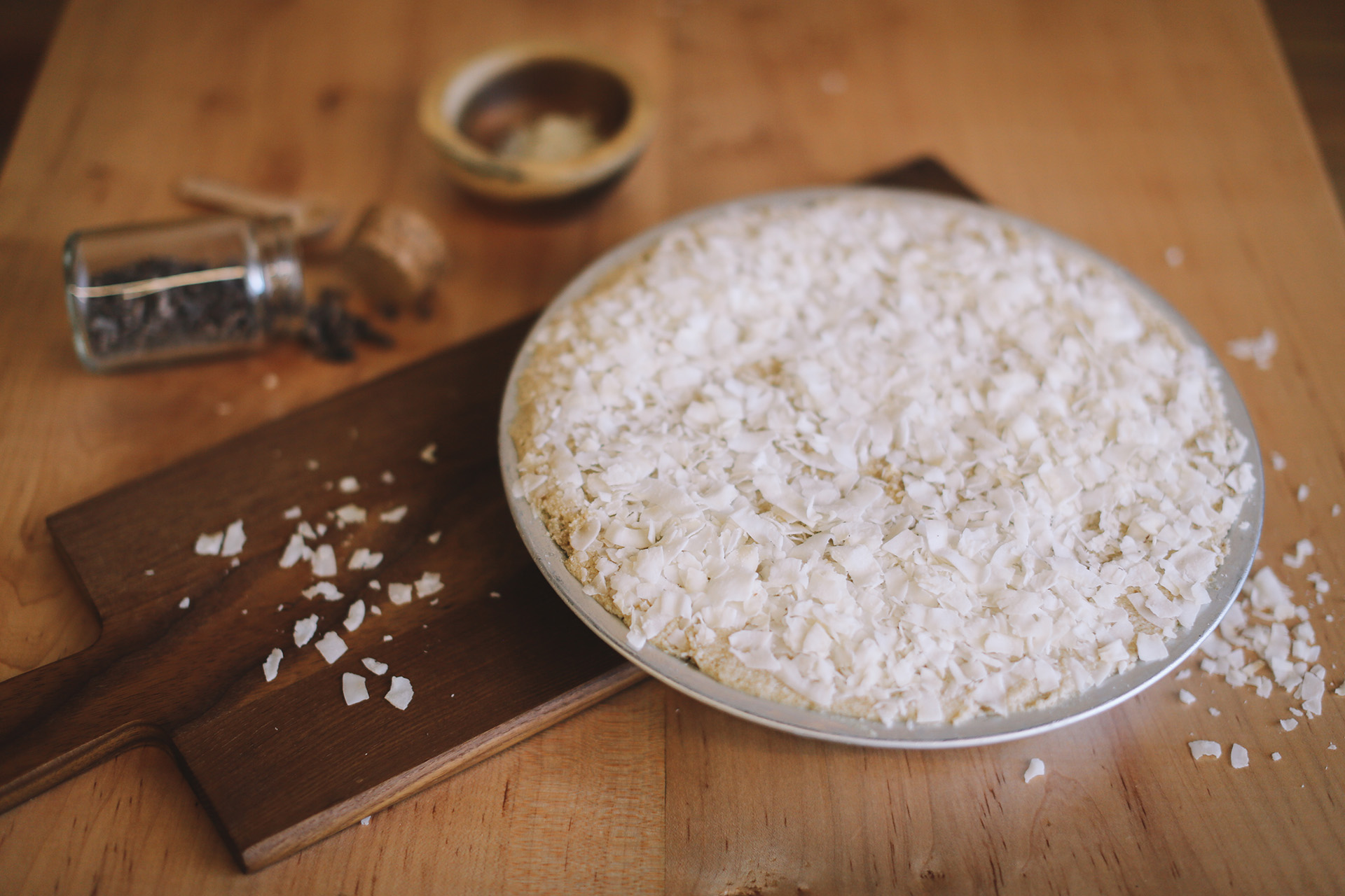 Uncut coconut cream pie topped with shredded coconut on a pie plate on a wooden cutting board.