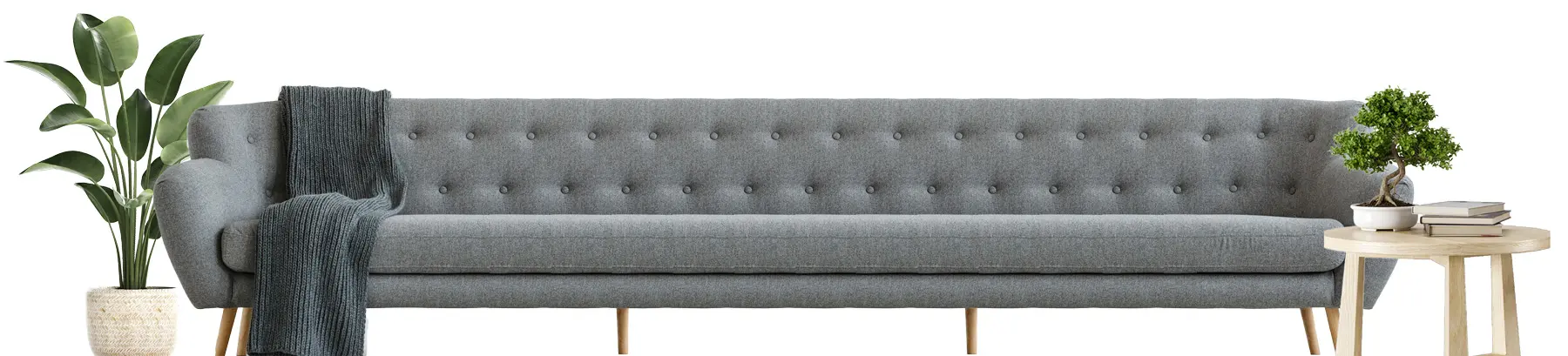 A long gray couch with a plant on the left and a table with books on the right.
