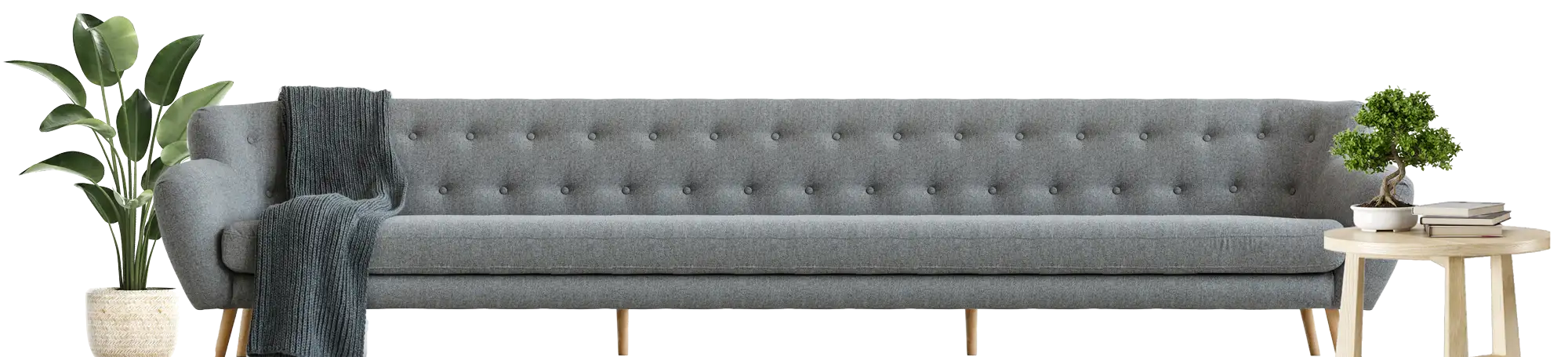 A long gray couch with a plant on the left and a table with books on the right.