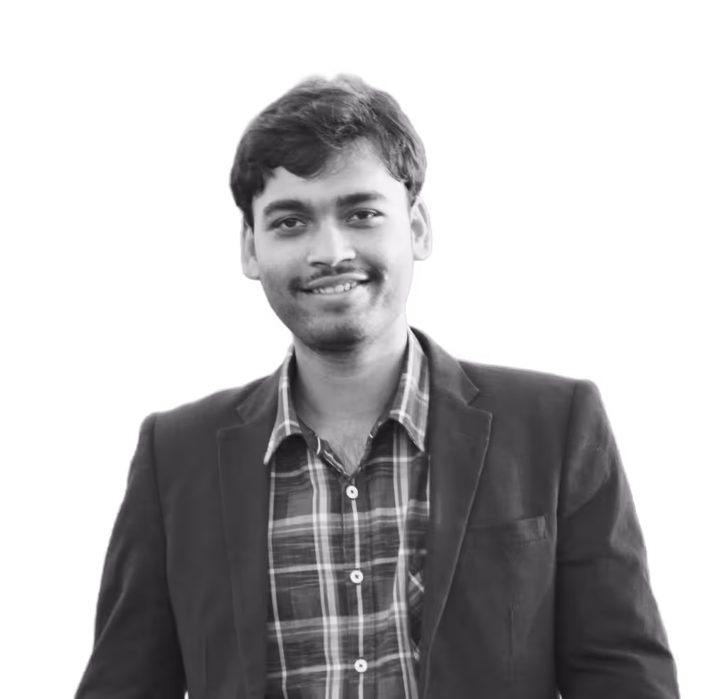 Smiling young man with short hair wearing a plaid shirt and dark blazer.