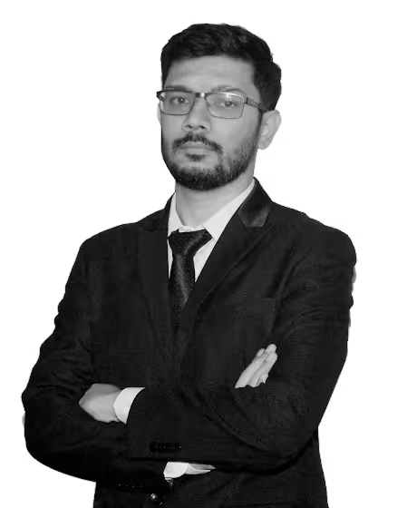 Man with beard and glasses wearing a black suit and tie with arms crossed, looking confidently at the camera.