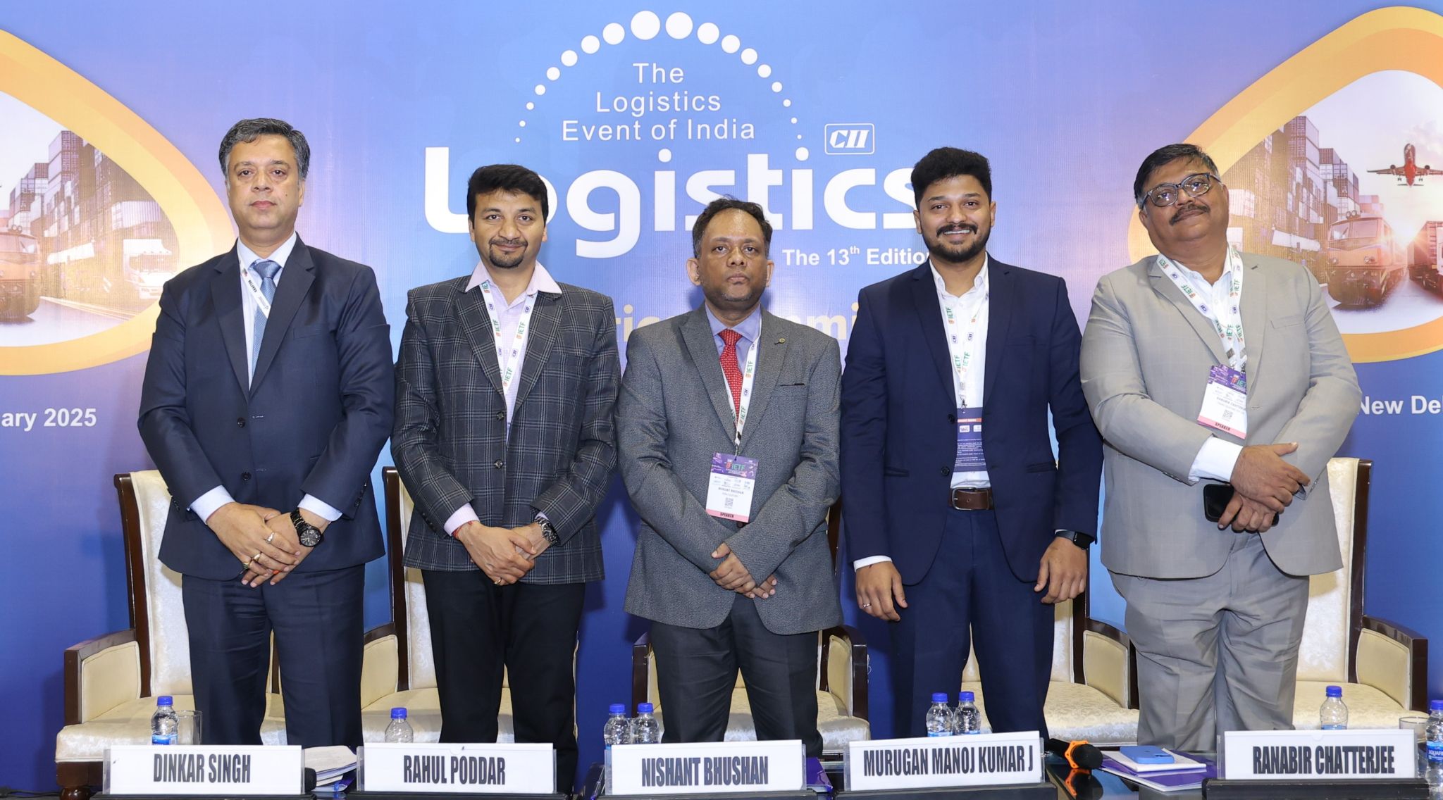 Five men in business attire standing behind chairs with nameplates at a logistics event in India.