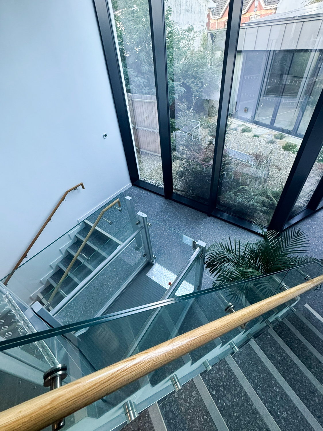Modern indoor wheelchair lift next to a staircase with glass panels and wooden handrails.