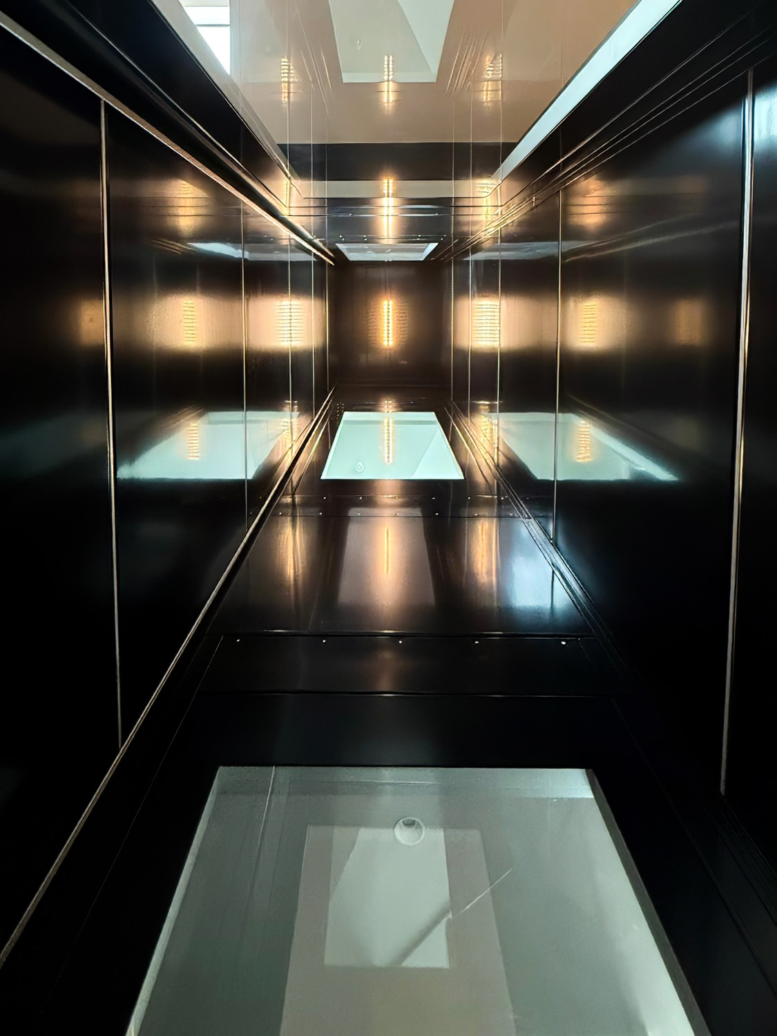 Interior view of a modern elevator shaft with dark metallic walls and illuminated panels reflecting light.