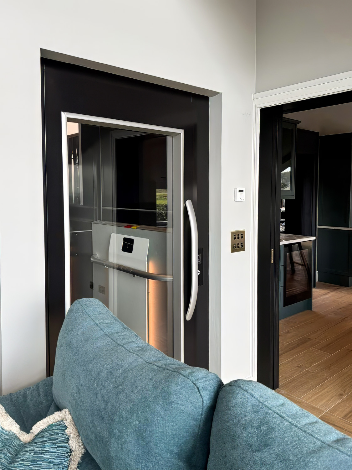 Light blue sofa with textured pillows next to an elevator with a black and white door and a side table with books.