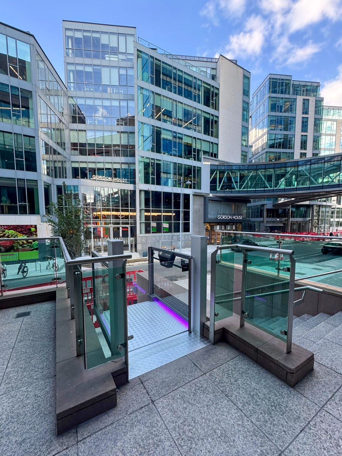Modern wheelchair lift platform with metal floor and control panel, overlooking outdoor stairs and glass railing.