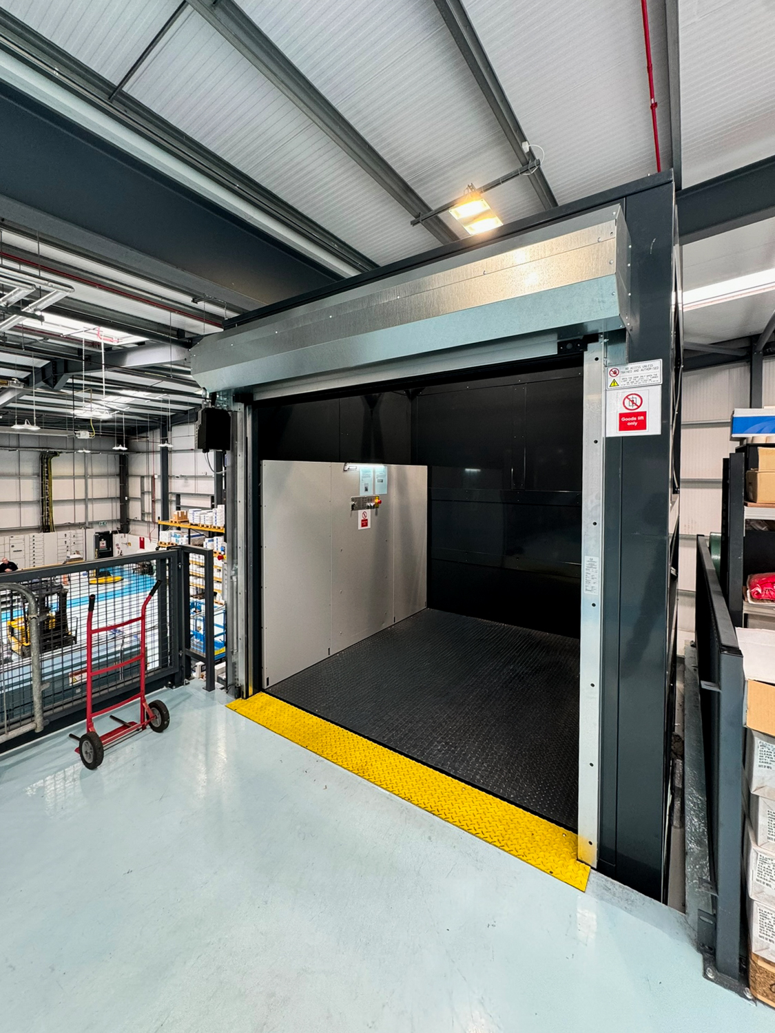 Empty industrial goods lift with metal floor and yellow threshold in a warehouse setting.