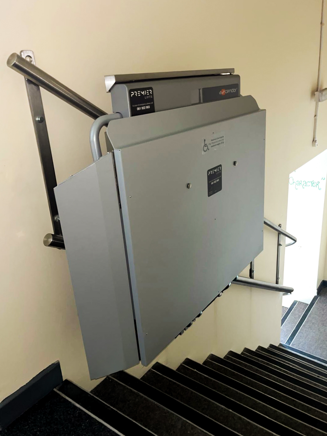 Folded gray wheelchair lift installed along a stairway with metal handrails.