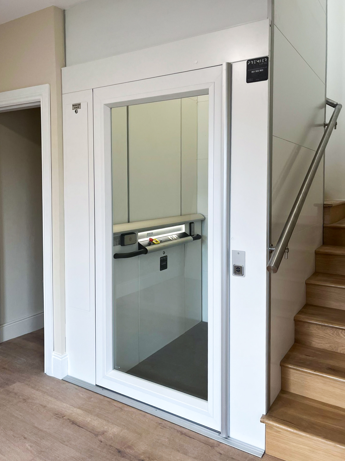 Modern white platform lift installed next to wooden stairs inside a building.