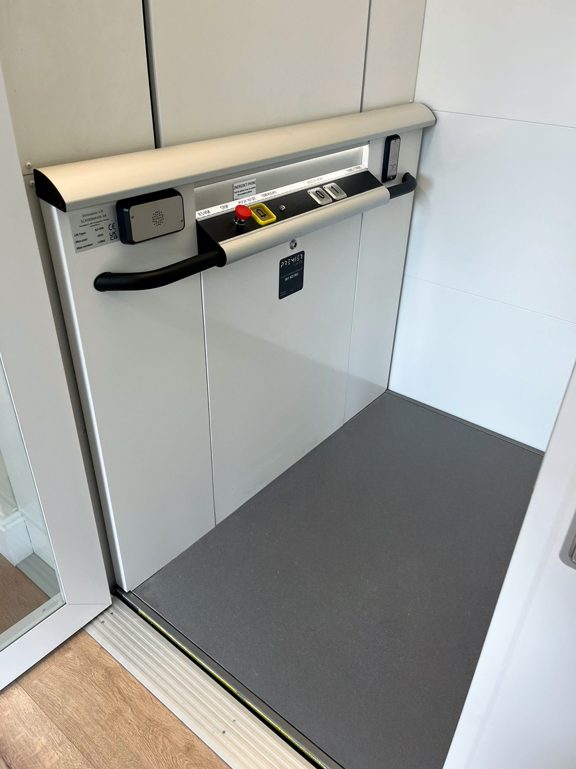 Interior of a modern wheelchair-accessible platform lift with control panel and safety handrails.