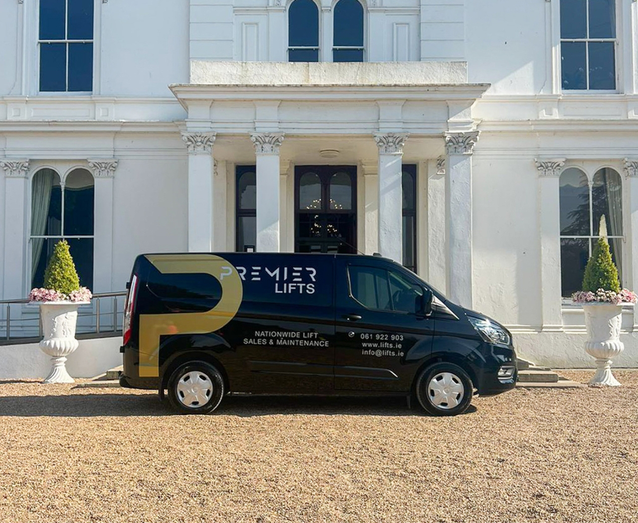 Black Premier Lifts van parked in front of a white classical building with columns and large windows.