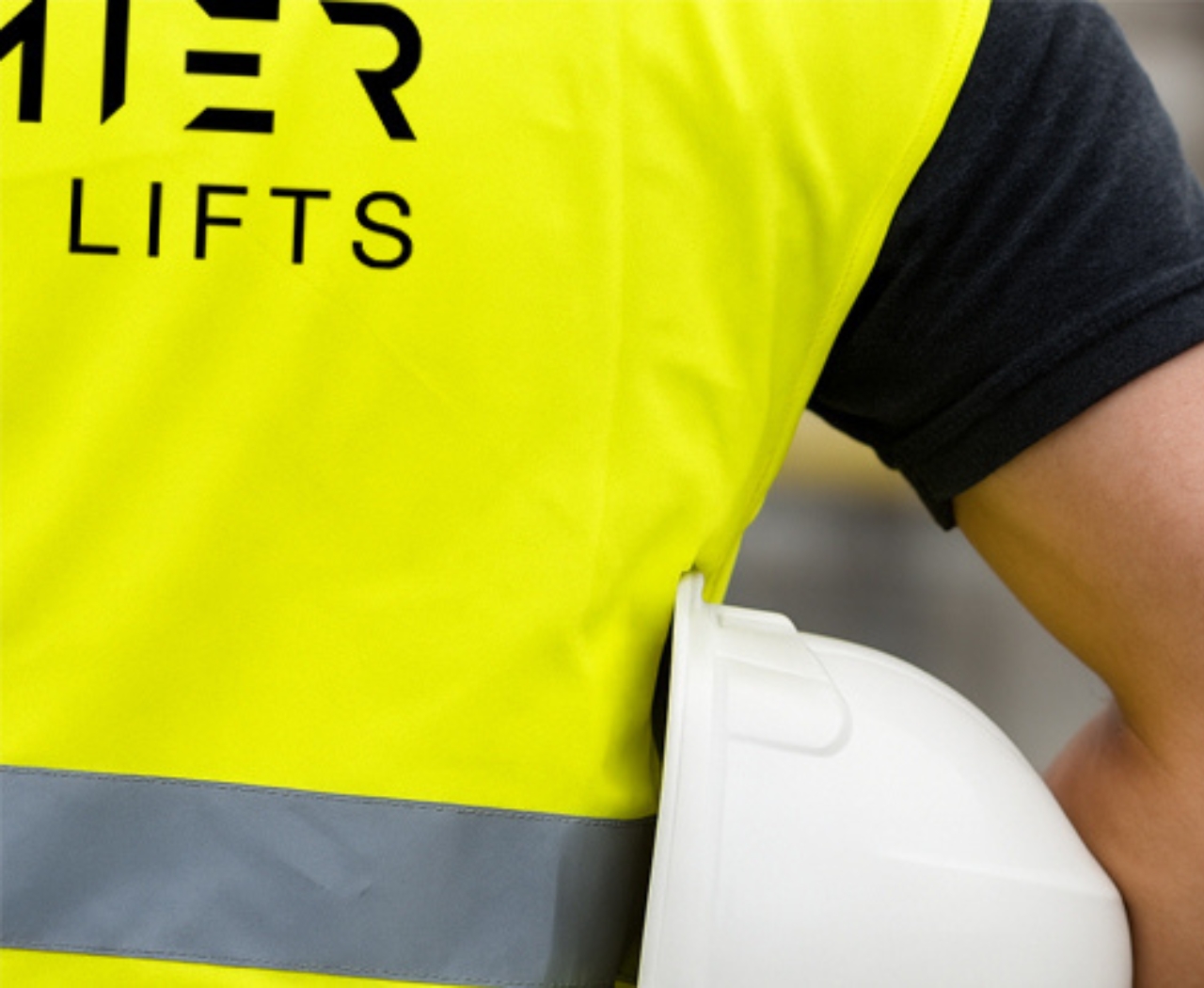 Person wearing high-visibility yellow vest with 'LIFTS' text holding a white construction helmet.