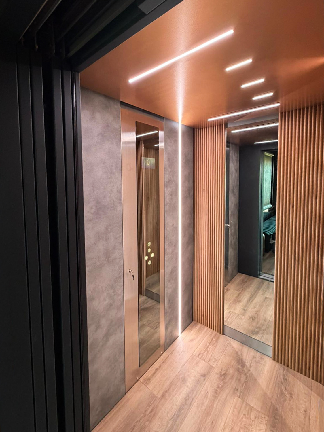 Modern eco home lift elevator interior with wood paneling, vertical LED strip light, and a large mirror on the right wall reflecting a window and seating.