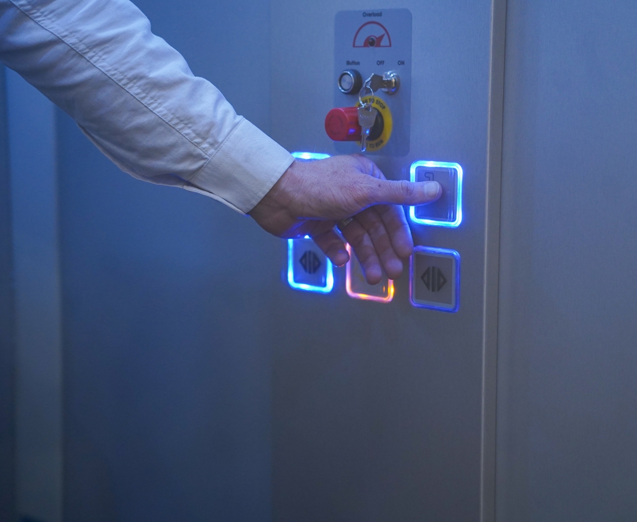 Man in a black Premier Lifts jacket pressing the down button for an elevator.