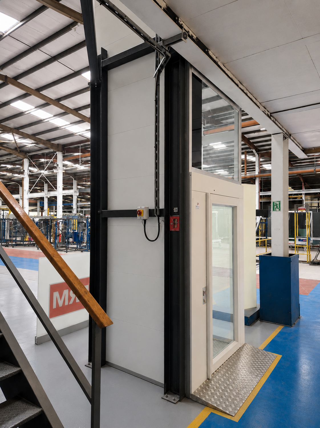 Glass platform lift with metal ramp inside a spacious industrial warehouse.