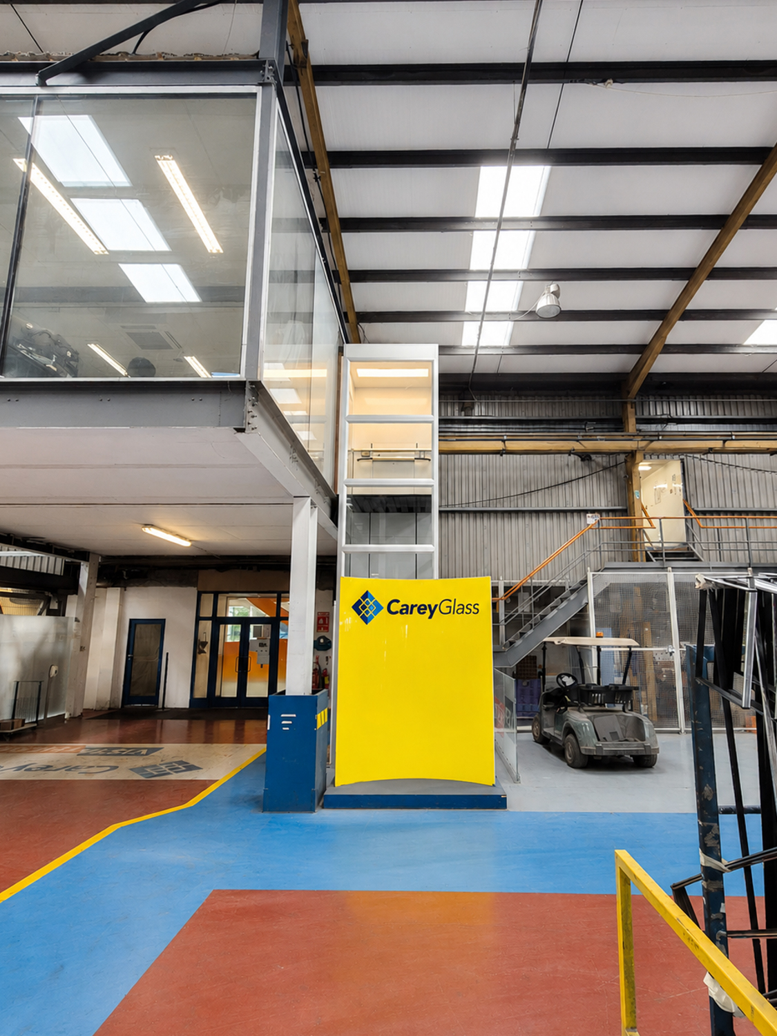 Industrial interior with a CareyGlass branded yellow platform lift and a parked golf cart.